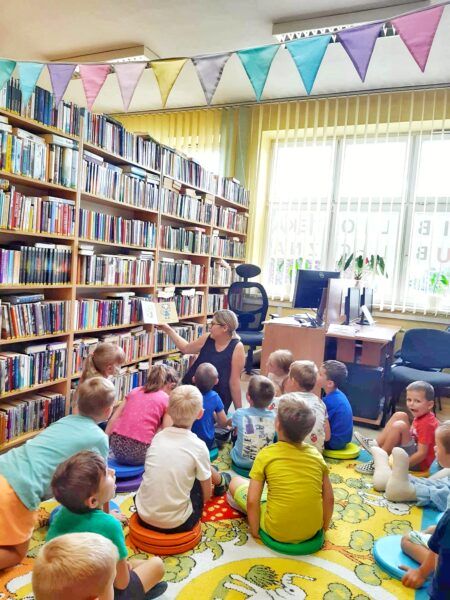 Bibliotekarka czyta dzieciom ksiązkę, wszyscy siedzą na dywanie